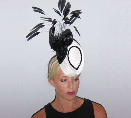 An Ascot  Statement head piece that’s a mystery how it stands up. Shown in White Sinamay and trimmed in Black Swiss Braid and Feathers.