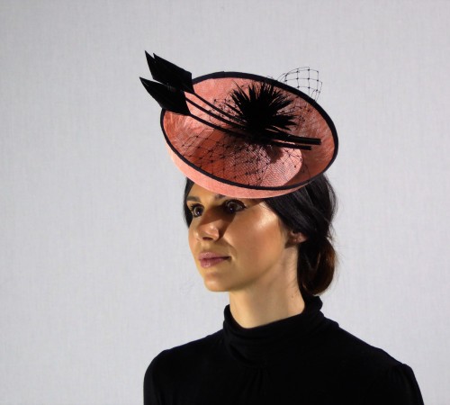 Small saucer cocktail hat in apricot sinamay, black feather and spiked flower.